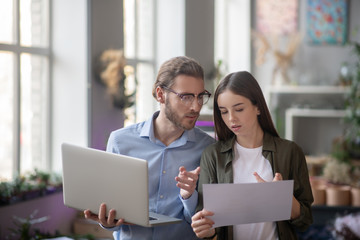 Man with a laptop and girl with scheme standing in office.