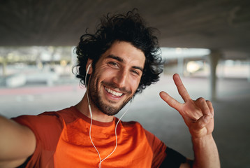 Close-up portrait of handsome positive cheerful fitness man pulling a peace sign to the camera