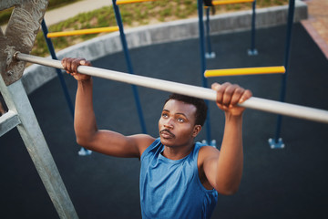 Strong fit young african american man doing pull-ups on a bar in a park - outdoor gym