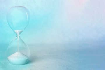 Time concept. An hourglass with the period coming to an end, with copy space, in teal blue, toned image