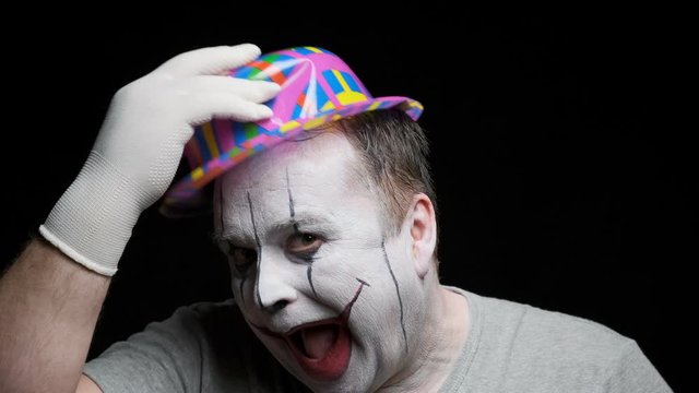 cheerful clown with terrible makeup on his face greets audience in circus on black background.