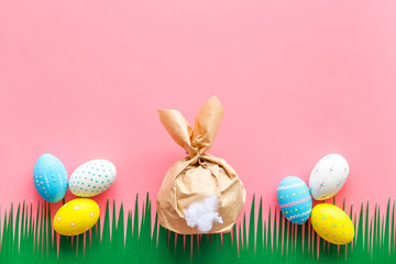 Easter symbols. Bunny and painted eggs on grass on pink background top-down frame copy space