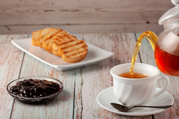 Freshly made tea in a teapot with cookies and jam on the table