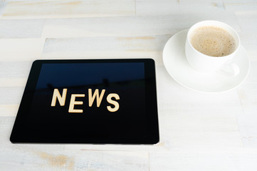 A tablet computer with the word news on a wooden table, next to it a cup of coffee
