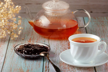 Freshly made tea in a teapot with cookies and jam on the table