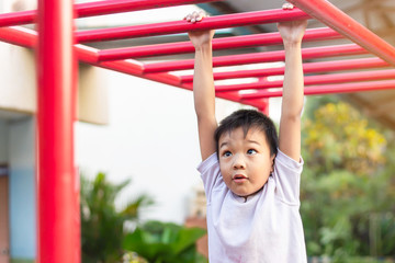 Fototapeta premium Kid exercise for health and sport concept. Happy Asian student​ child boy playing and hanging from a steel bar at the playground. 5-6 years old.