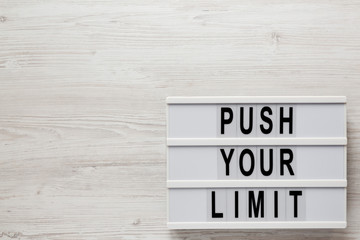 'Push your limit' words on a lightbox on a white wooden background, top view. Overhead, from above, flat lay. Copy space.