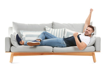 Young man listening to music while lying on sofa against white background