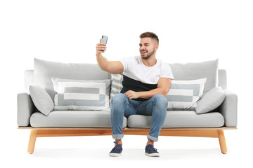 Young man taking selfie while sitting on sofa against white background