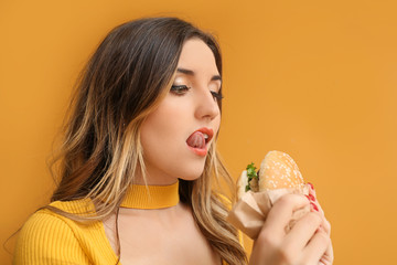 Portrait of beautiful young woman with burger on color background