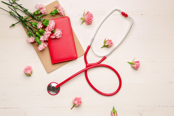 Stethoscope with flowers and notebooks on white wooden background