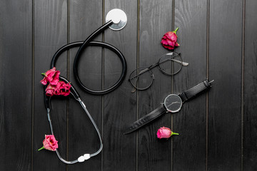 Stethoscope with flowers, clock and eyeglasses on dark wooden background