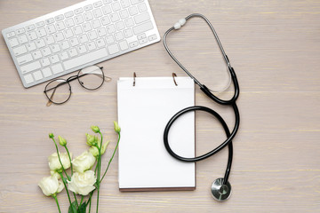 Stethoscope with notebook, computer keyboard and flowers on wooden background