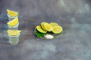 Three glass glasses of tequila with salt at the edges and slices of lime stand on a wooden table...