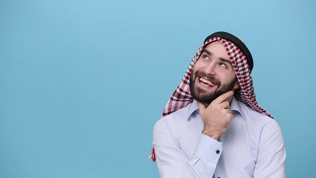 Bearded arabian muslim man 20s in keffiyeh kafiya ring casual clothes isolated on pastel blue background. People religious lifestyle concept. Pensive guy think hold index finger up with great new idea