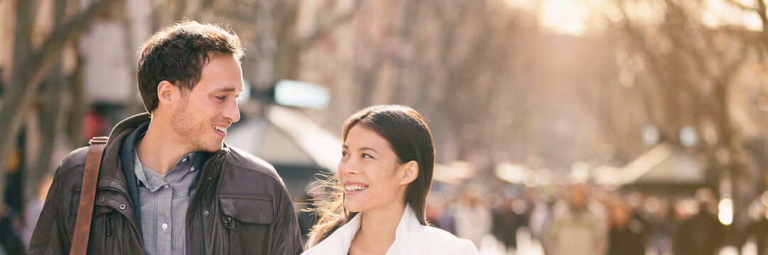 Happy couple falling in love walking in European city on spring travel vacation getaway smiling at each other panoramic background. Young tourists interracial relation lovers banner.