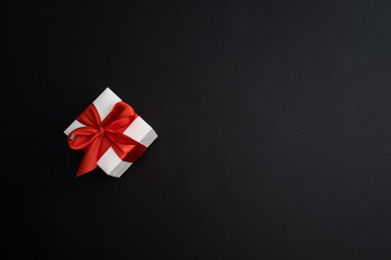 White gift box with red ribbon on dark black background.