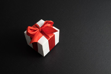 White gift box with red ribbon on dark black background.