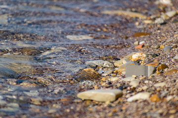Large and smooth stones in the coastal waves of salty sea water. The coast of the black sea foams and roars, beating against a huge pebble, illuminated by sunlight