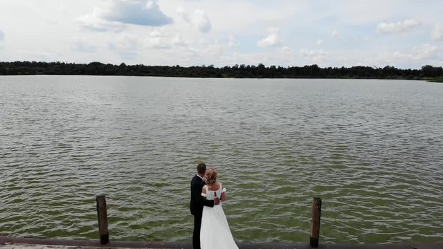 Aerial flight above of groom and bride hugging on wooden pier, flying over lake