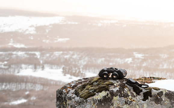 binoculars in the mountains lying on the edge of a cliff against a landscape with a sunset