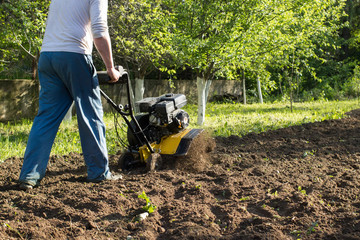 A perspective view of a man during soil plow process by motor cultivator