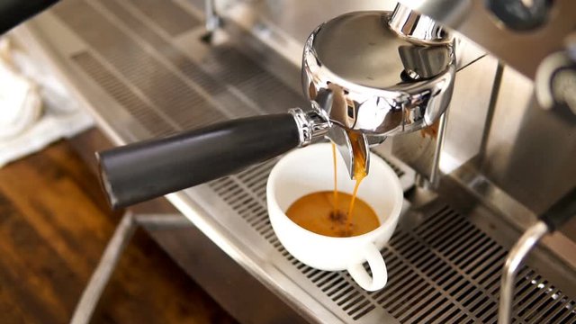 Coffee being brewed by the machine flowing through portafilter into the cup, slow motion shot