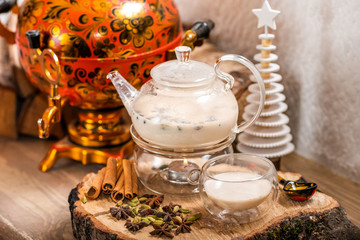 Traditional Indian tea in the teapot candle basking with milk and aromatic spices masala chai and cup on wooden background. Food and drink. New year holidays, christmas xmas concept