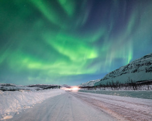 Northern lights over icy road with car headlights