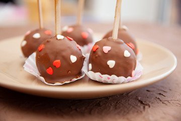 Chocolate candies covered with pink and red hearts on a stick lie on a white plate