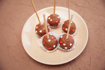 Chocolate candies covered with pink and red hearts on a stick lie on a white plate