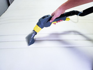 man's hand cleans a modern white mattress with a professional cleaning agent.