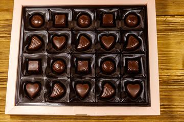 Assorted chocolate candies in a box on wooden table. Top view