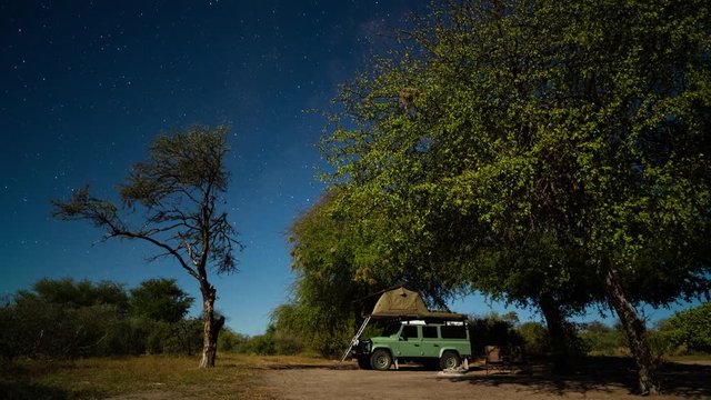 Static timelapse of adventurous couple on Africa Safari in Botswana Game Reserve, wild camping/glamping under moonlight night sky, tilt up to Miky Way.
