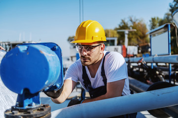 Handsome serious caucasian workman in overalls and with helmet on head pressing button on dashboard...