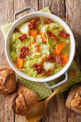 Tasty savoy cabbage soup with potatoes and fried bacon closeup in a bowl. Vertical top view