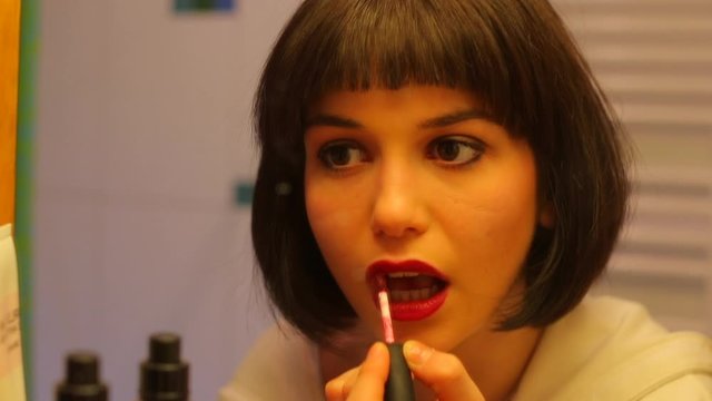 A young girl paints her lips with red lipstick.