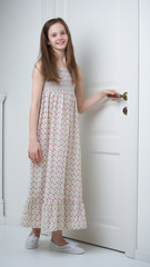 Girl teenager in a smart dress standing near the white door.