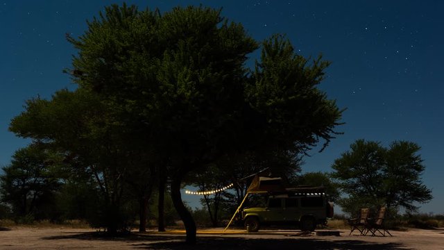 Static timelapse of rural campsite on African Safari in Botswana Game Reserve, wild camping/glamping under moonlight night sky with bonfire/fire and truck, tent and solar lights.