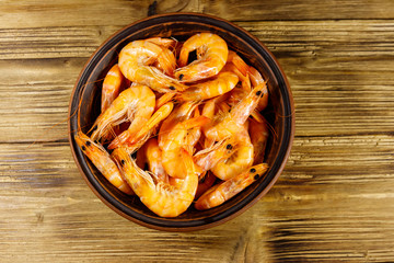 Fresh raw shrimps in a ceramic bowl on a wooden table. Top view