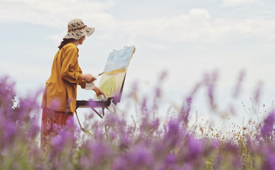 Girl artist is painting lavender field on the plein air. Box easel with canvas, oil paint, palette,...
