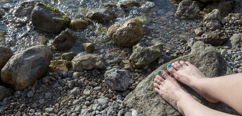 Female feet with colored pedicure on summer sea background. Rocky coast of the black sea. Panoramic banner. 