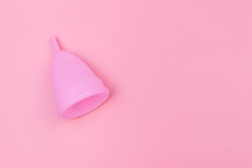 Pink reusable silicone menstrual cup on pink background. Top view, copy space. Concept of feminine hygiene, gynecology and health