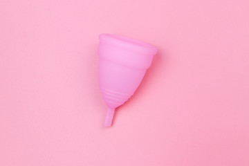 Pink reusable silicone menstrual cup on pink background. Top view. Concept of feminine hygiene, gynecology and health