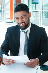 Fototapeta premium Happy business man discussing issues with partner in cafe. Business man sitting and talking with person who is out of view with building glass wall in background. Business issues concept.