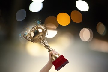 Human hand holding golden trophy on bokeh  background