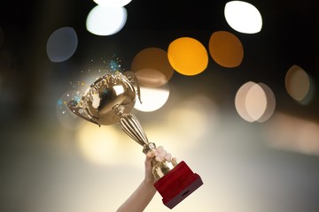 Obraz premium Human hand holding golden trophy on bokeh background