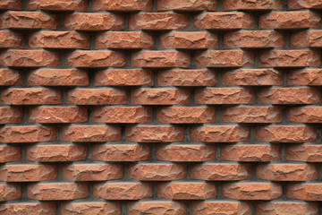 Embossed brown-colored grungy brick wall, lined with separate rough and hewn bricks. The fragment of a new decorative bricklaying. The design of stylish exterior