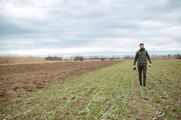 Young farmer on the field controls the growth of plants