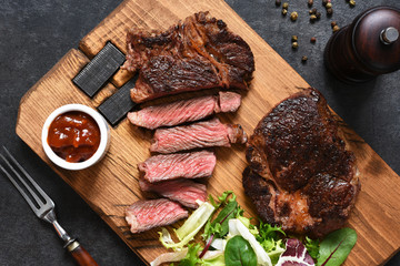 Grilled marbled beef steak with salad on a wooden board on the kitchen table. With copy space under the text.